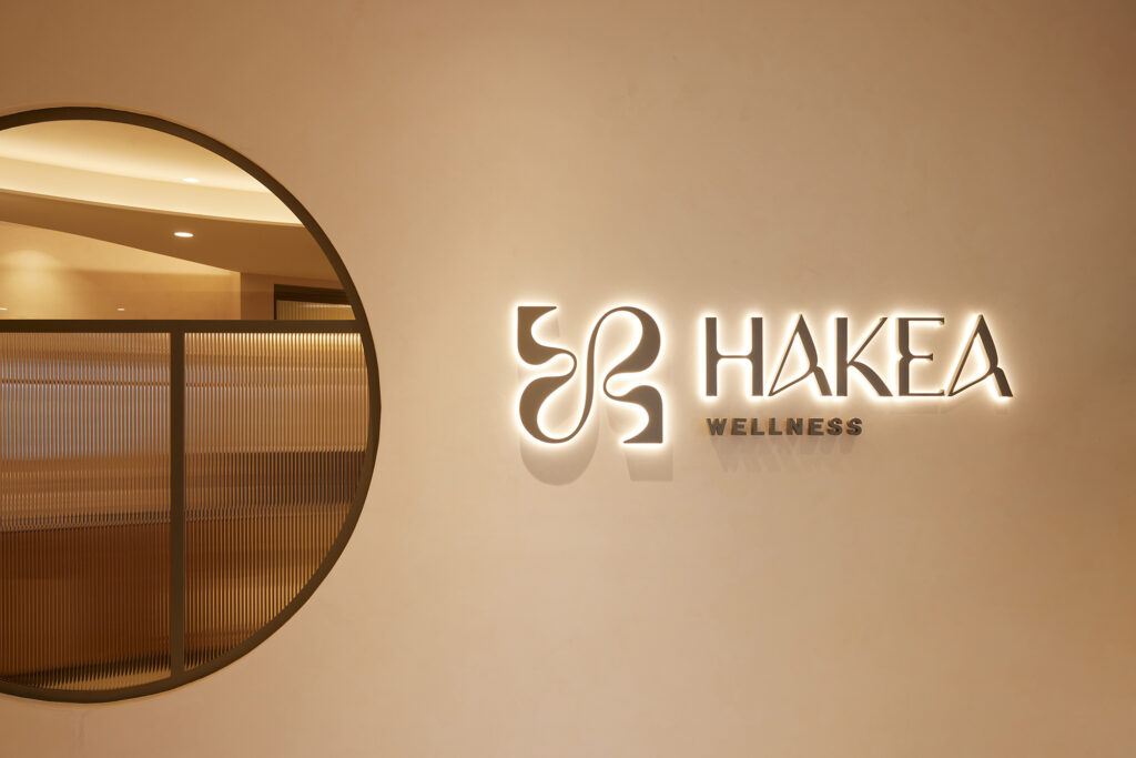 Hakea Wellness logo backlit sign, circular window, fluted glass, bronze frame, white wall, modern bright clean interior
