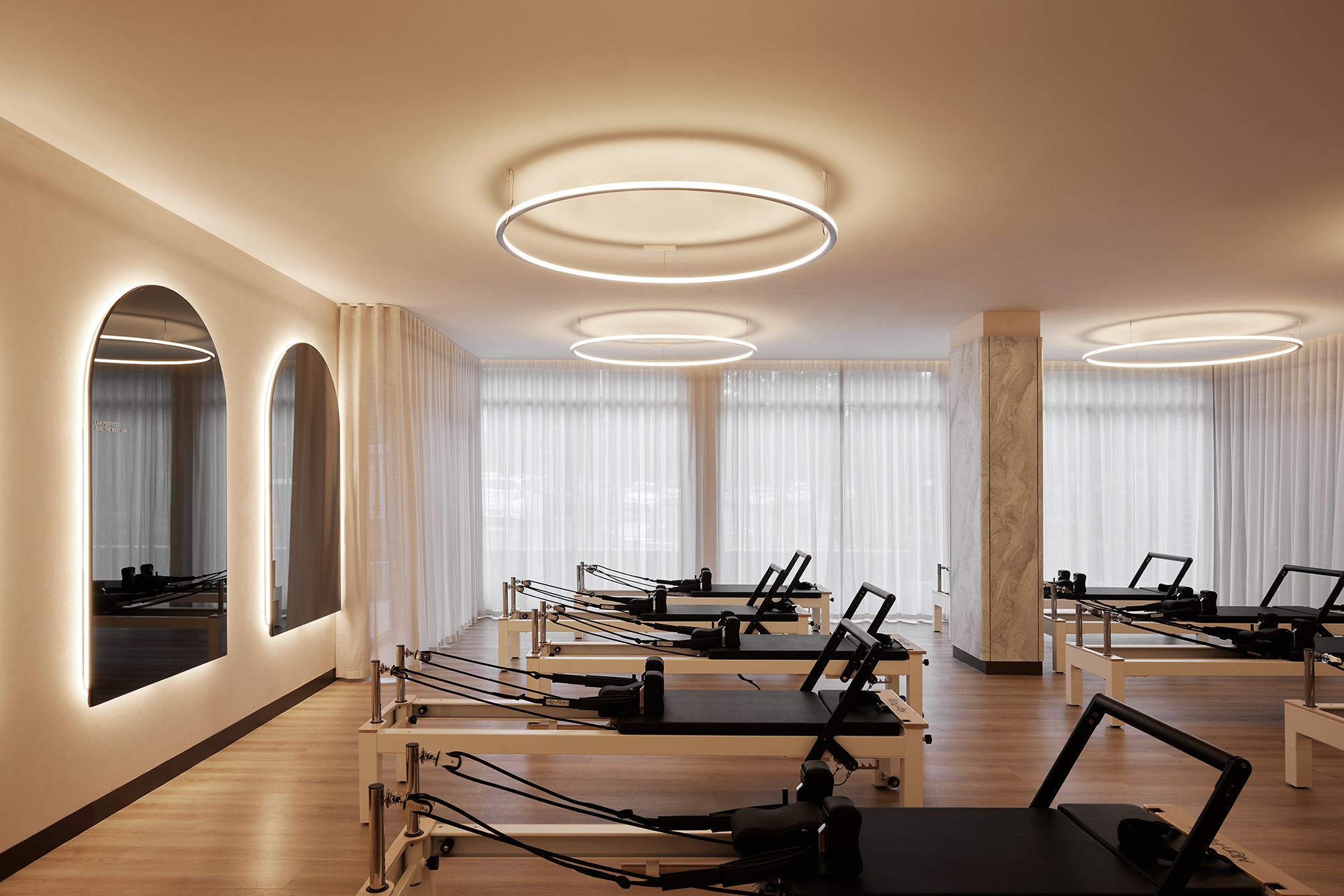 modern bright interior reform pilates, marble column, timber floor, back-lit arched mirrors, sheer curtains, LED ring lights